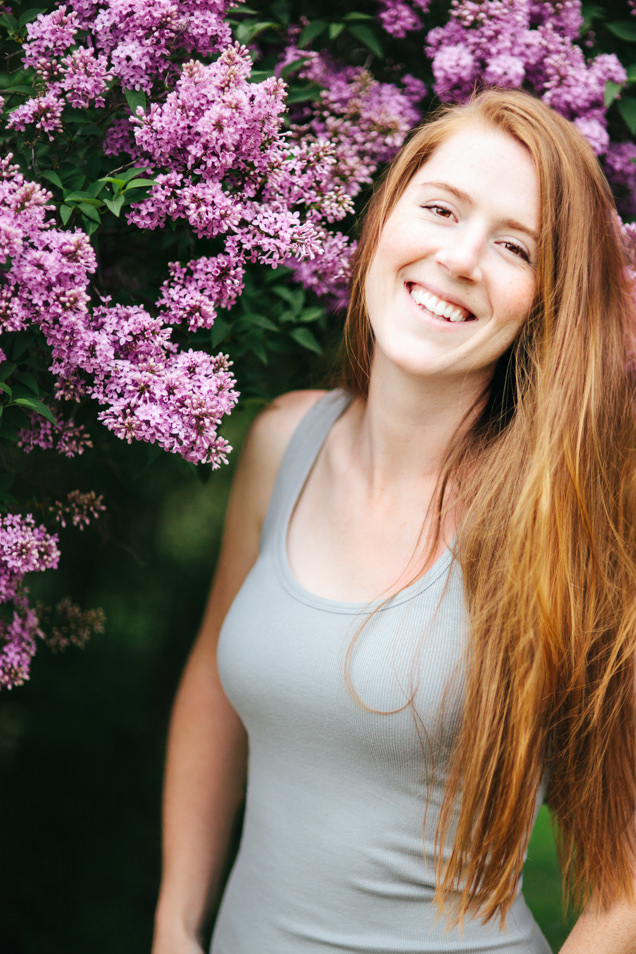 Kristine Paulsen smiles in front of flowering lilacs