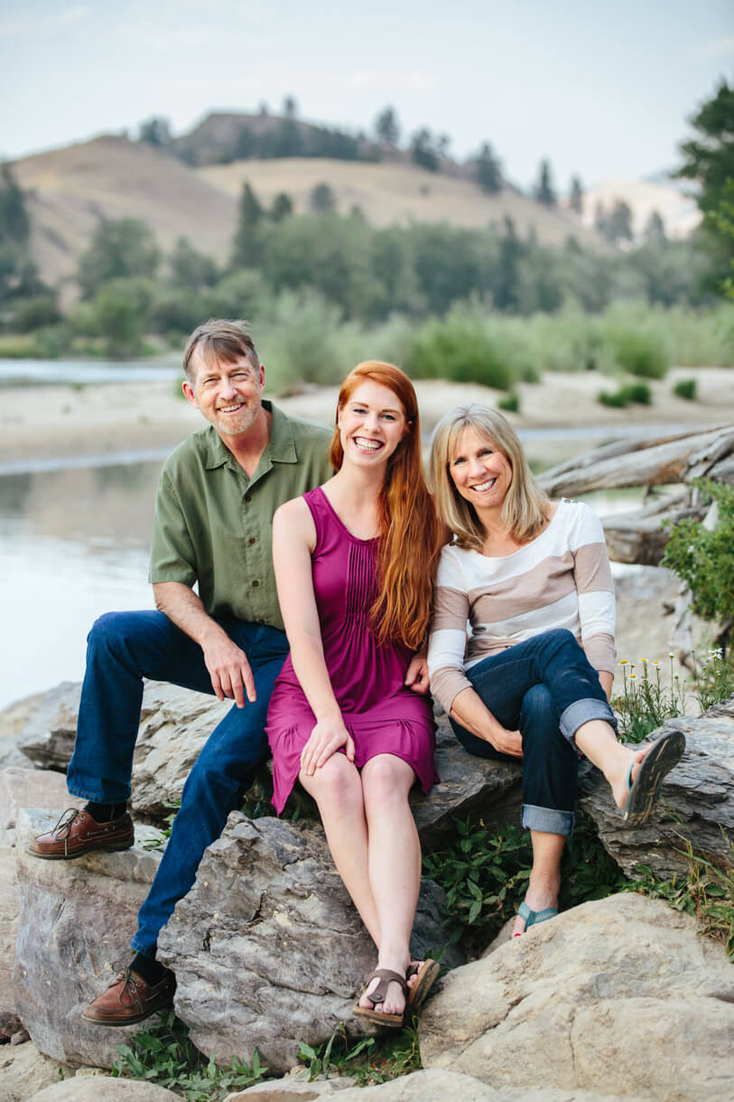 A mother, father and their daughter smile together and sit upon rocks during their family photos in Missoula Montana
