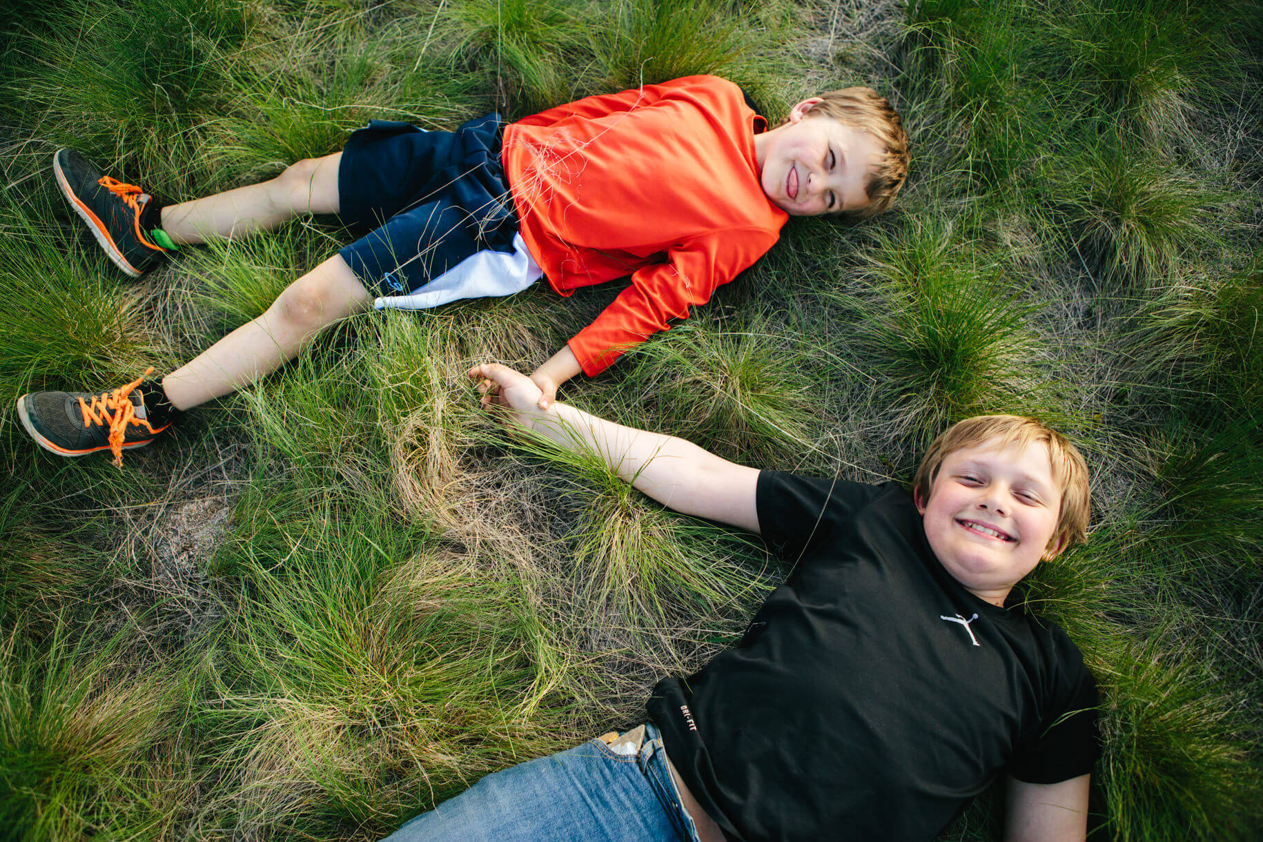 Two brothers hold hands and grin in the grass during their family portraits in Missoula Montana