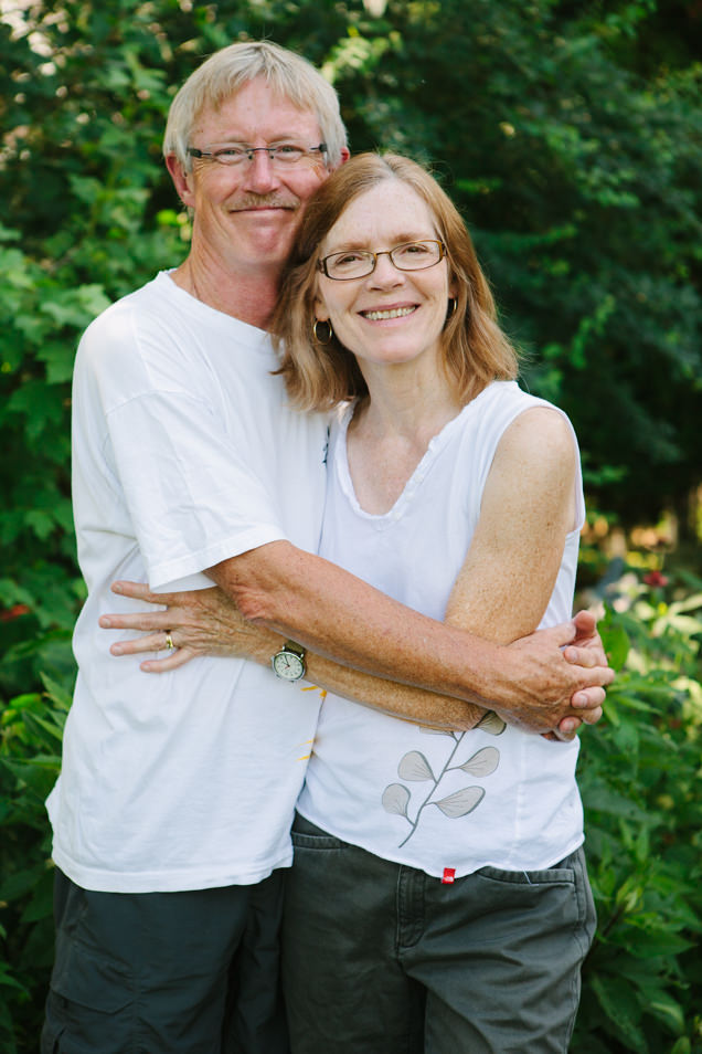 A husband and wife hug in front of greenery in their front yard