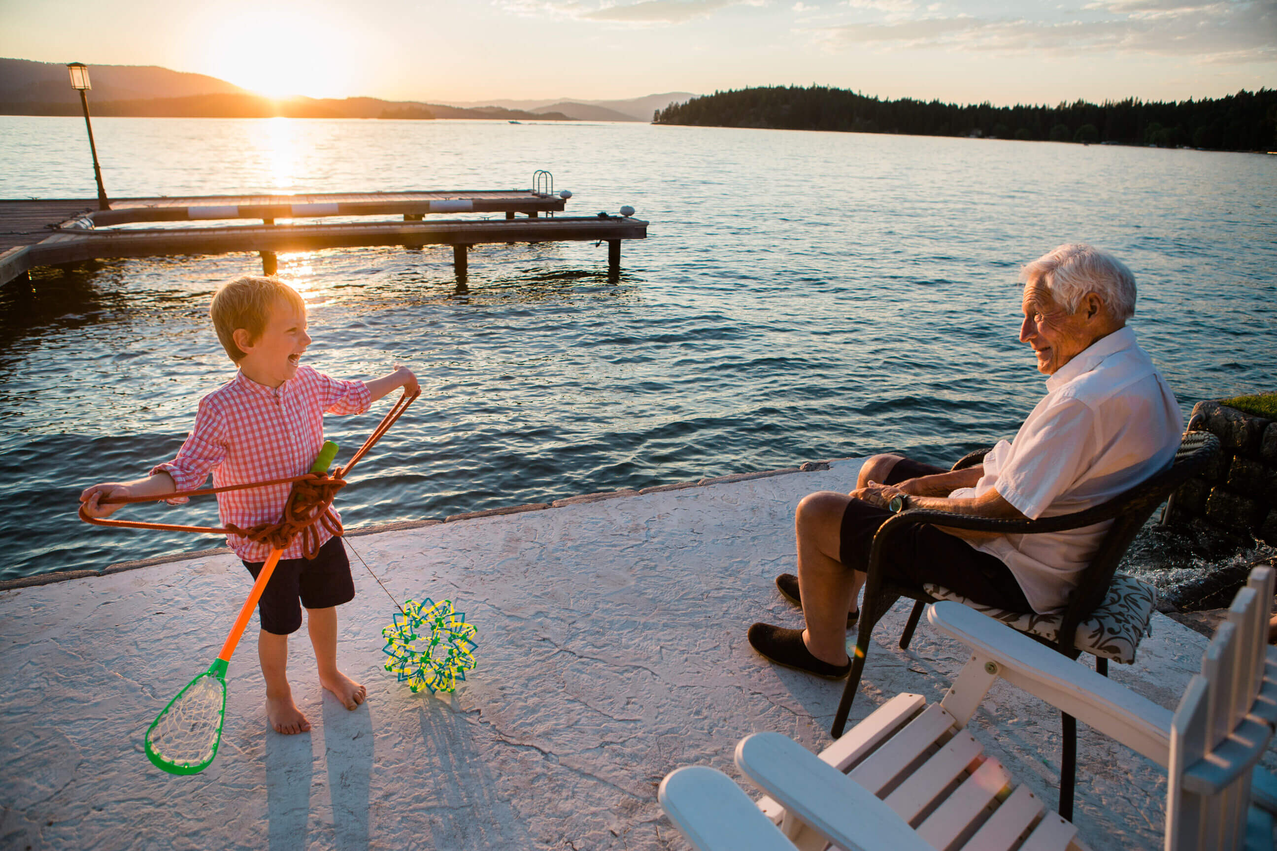A boy laughs with his grandfather at sunset on Flathead Lake during their family photo session in Polson Montana