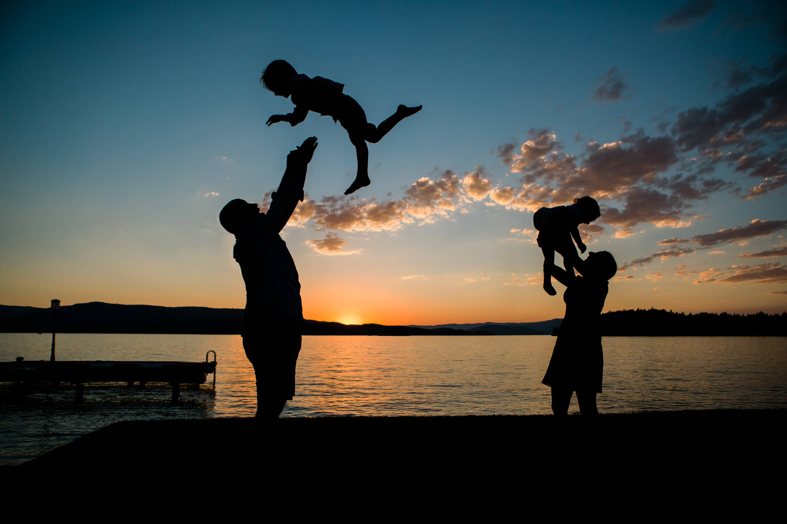 A father and mother toss their small children into the air during their family session on Flathead Lake in Montana at sunset