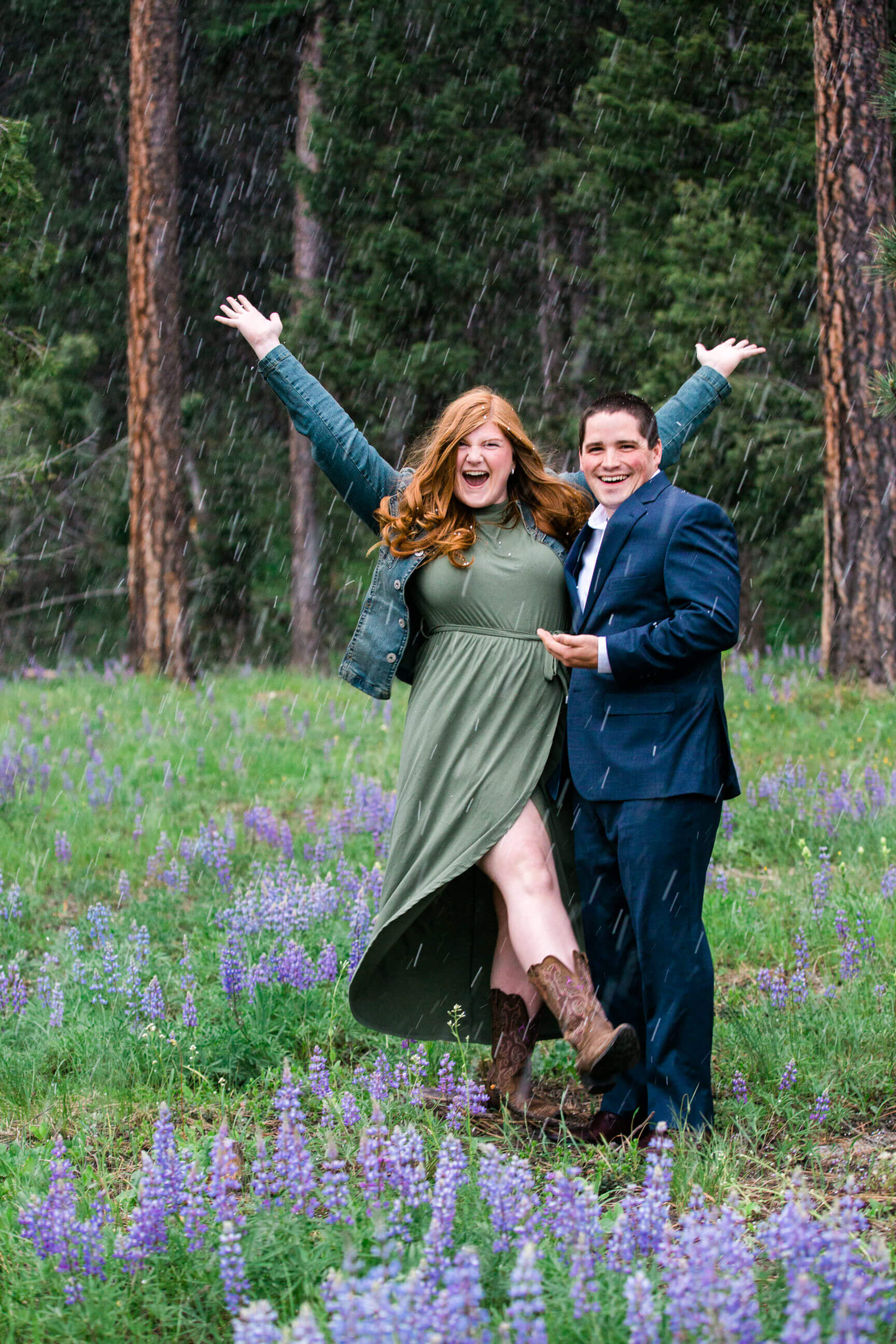 A husband and wife smile and laugh amidst a field of lupine wildflowers during a hail storm in Seeley Lake Montana