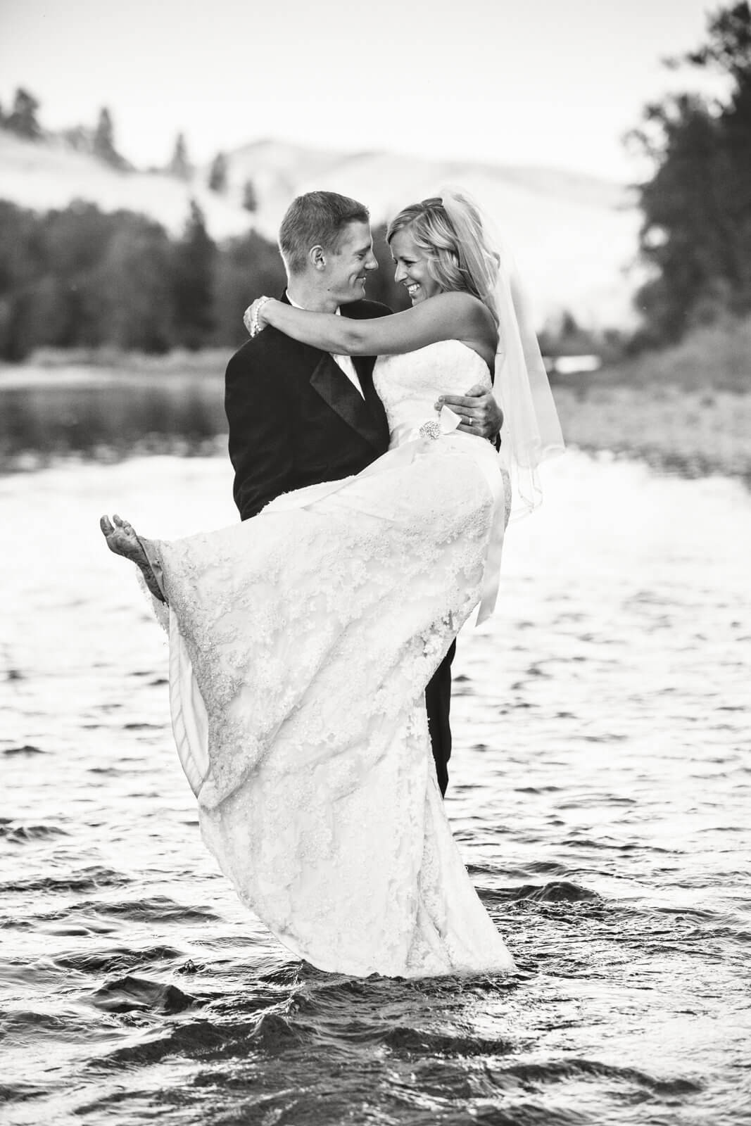 A groom holds his bride while standing in a river during their rock the dress session in Missoula Montana