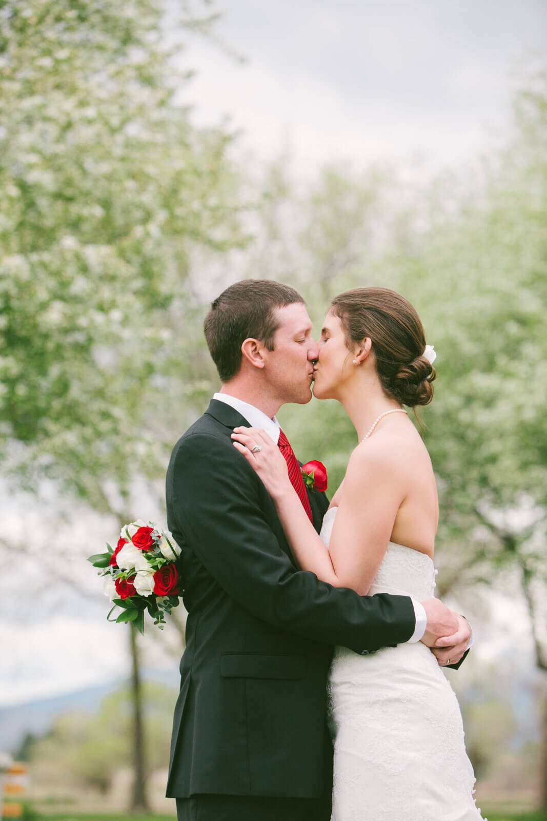 A bride and groom kiss in front of flowering fruit trees during their wedding at Fort Missoula in Missoula Montana