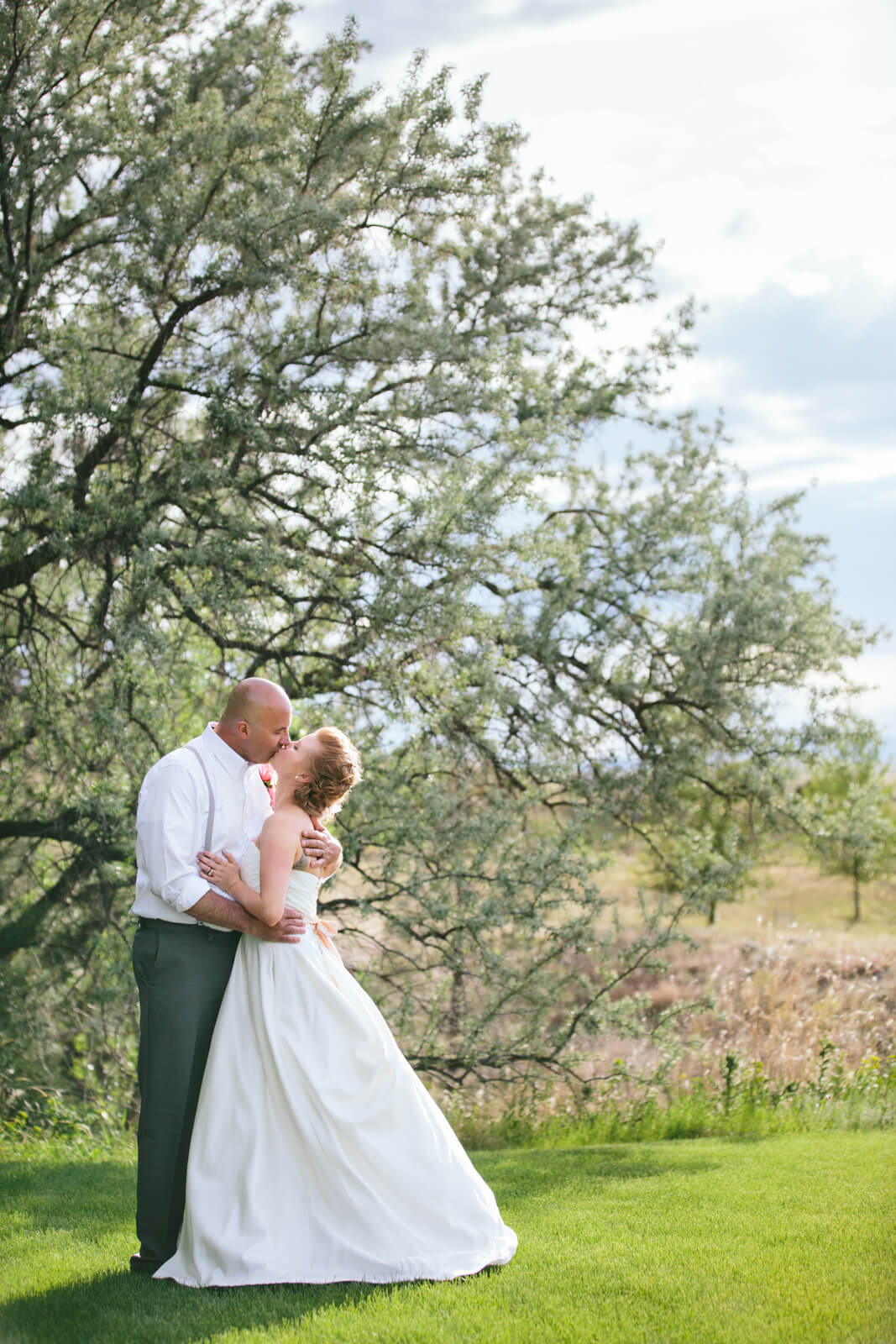 A bride and groom kiss in front of a tree during their wedding at the Lakeside Ranch in Helena Montana