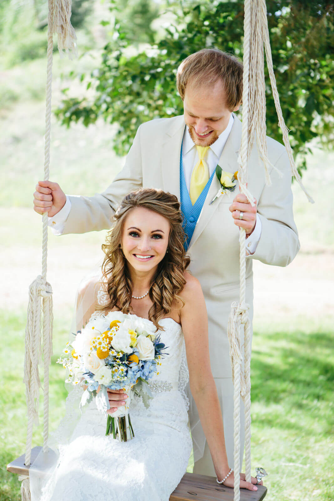 A bride holds her bouquet and sits on an old rope swing as her husband looks at her during their wedding in Great Falls Montana