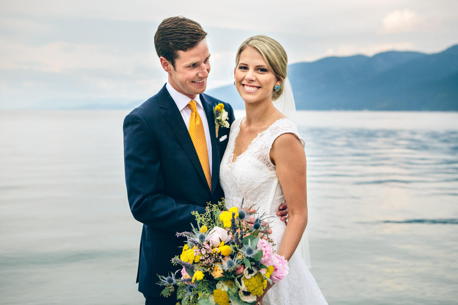 A groom smiles at his bride as they stand in front of Flathead Lake during their wedding at The Barn on Finley Point in Polson Montana