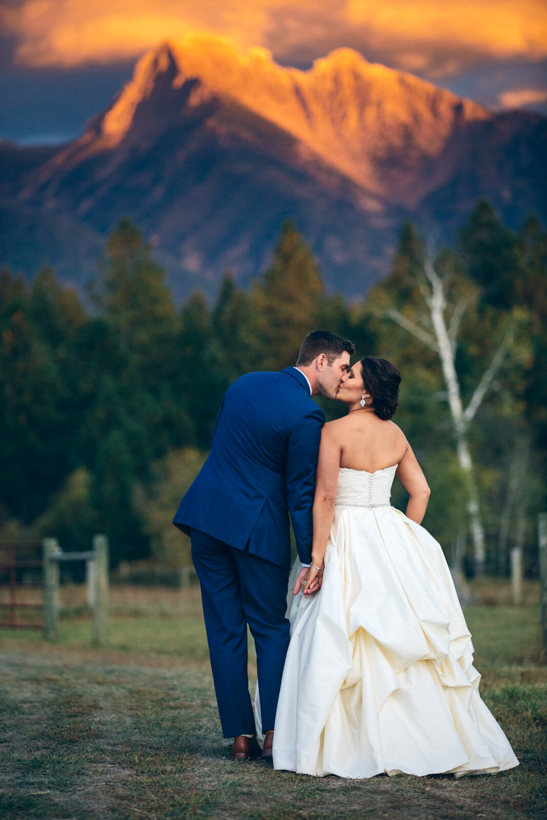 A groom kisses his bride in front of mountains during sunset at their wedding at Sky Ridge Ranch in Ronan Montana. 