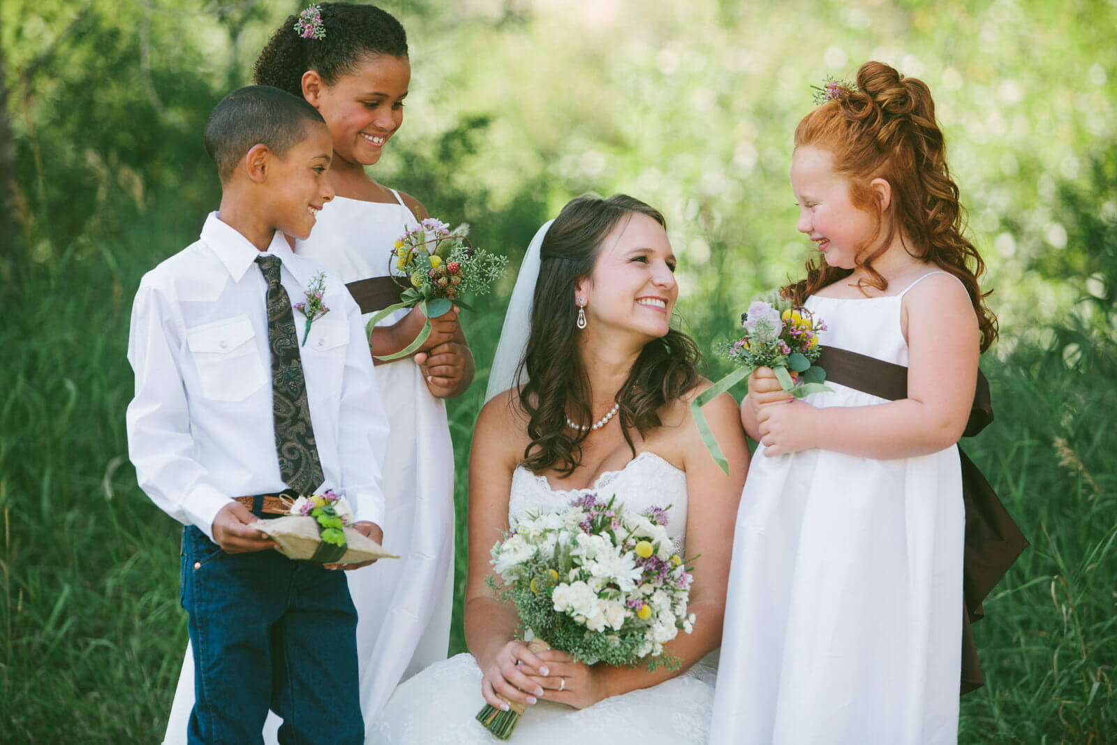 A bride smiles at her flower girls and ring bearer during her Darby Montana wedding