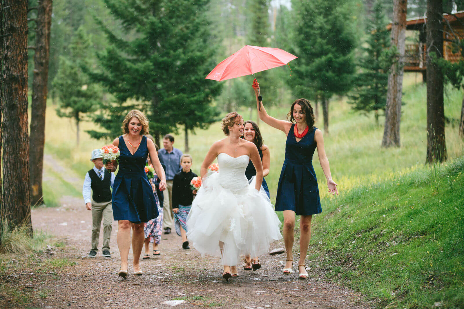 A bridesmaid holds an umbrella over a bride as they walk during her wedding day at the Double Arrow Lodge in Seeley Lake Montana