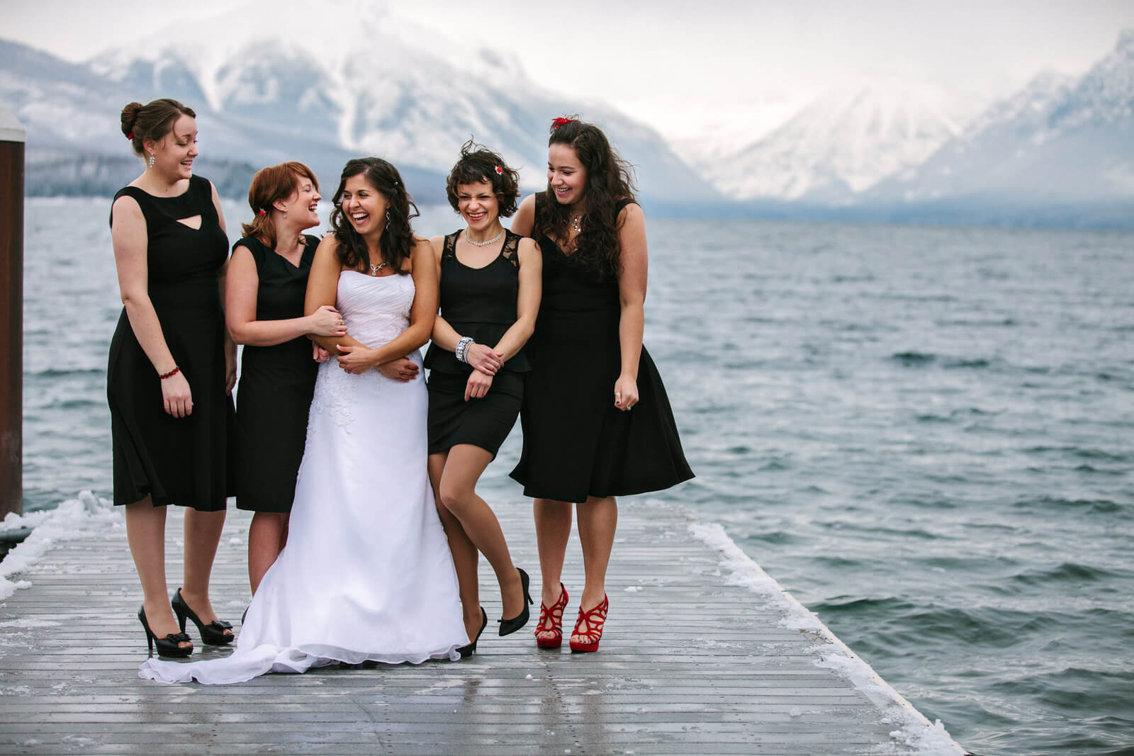 A bride and her bridesmaids laugh at Lake McDonald in Glacier during her winter wedding