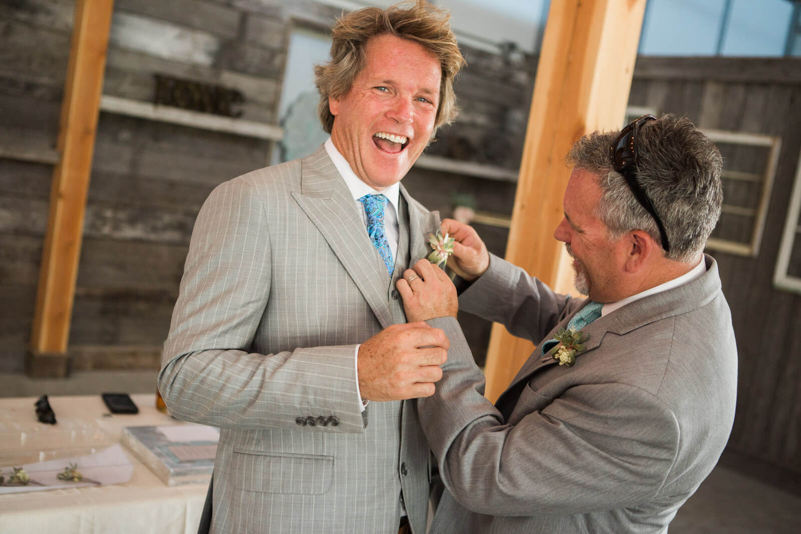 A groom laughs as his brother pins on his boutonnière during his wedding day at Sky Ridge Ranch in Ronan Montana