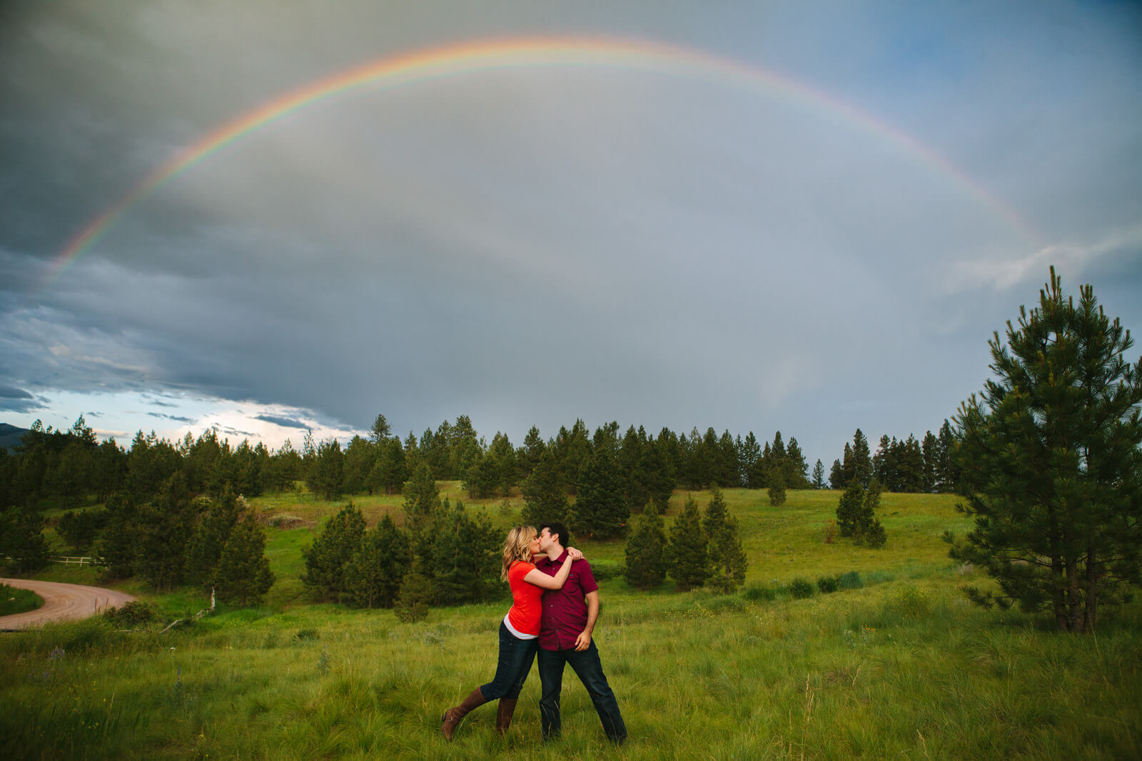 A couple kiss under a rainbow in Missoula Montana during their engagement session
