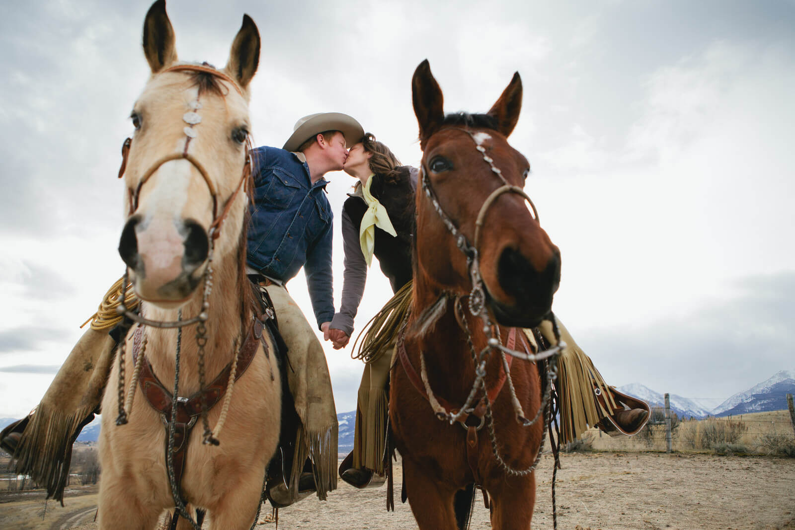 An engaged couple kiss while sitting on their horses in Montana