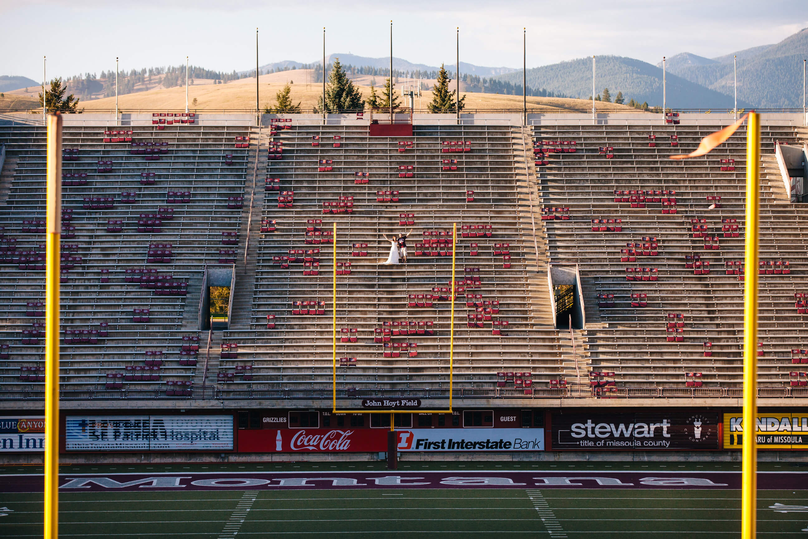 A bride and groom cheer in the bleachers of the University of Montana Grizzly stadium during their rock the dress photos in Missoula Montana