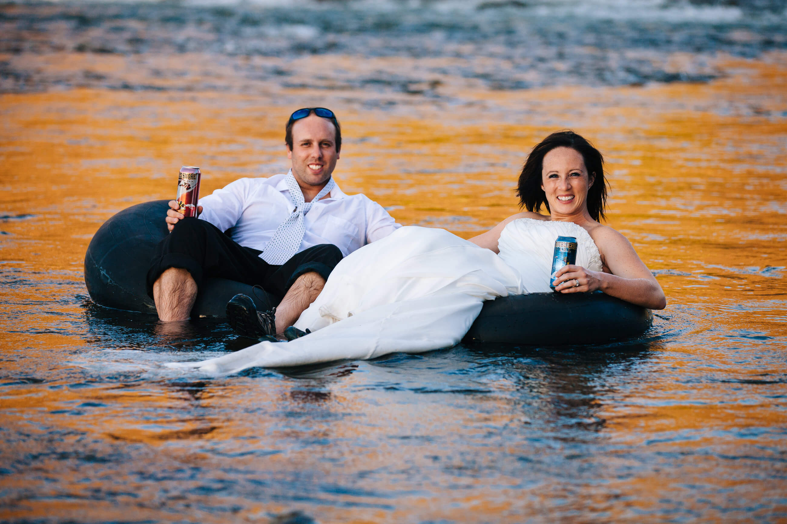A newly married couple floats down the Clark Fork River in their wedding dress and suit with Kettle House beers during their rock the dress photos in Missoula Montana