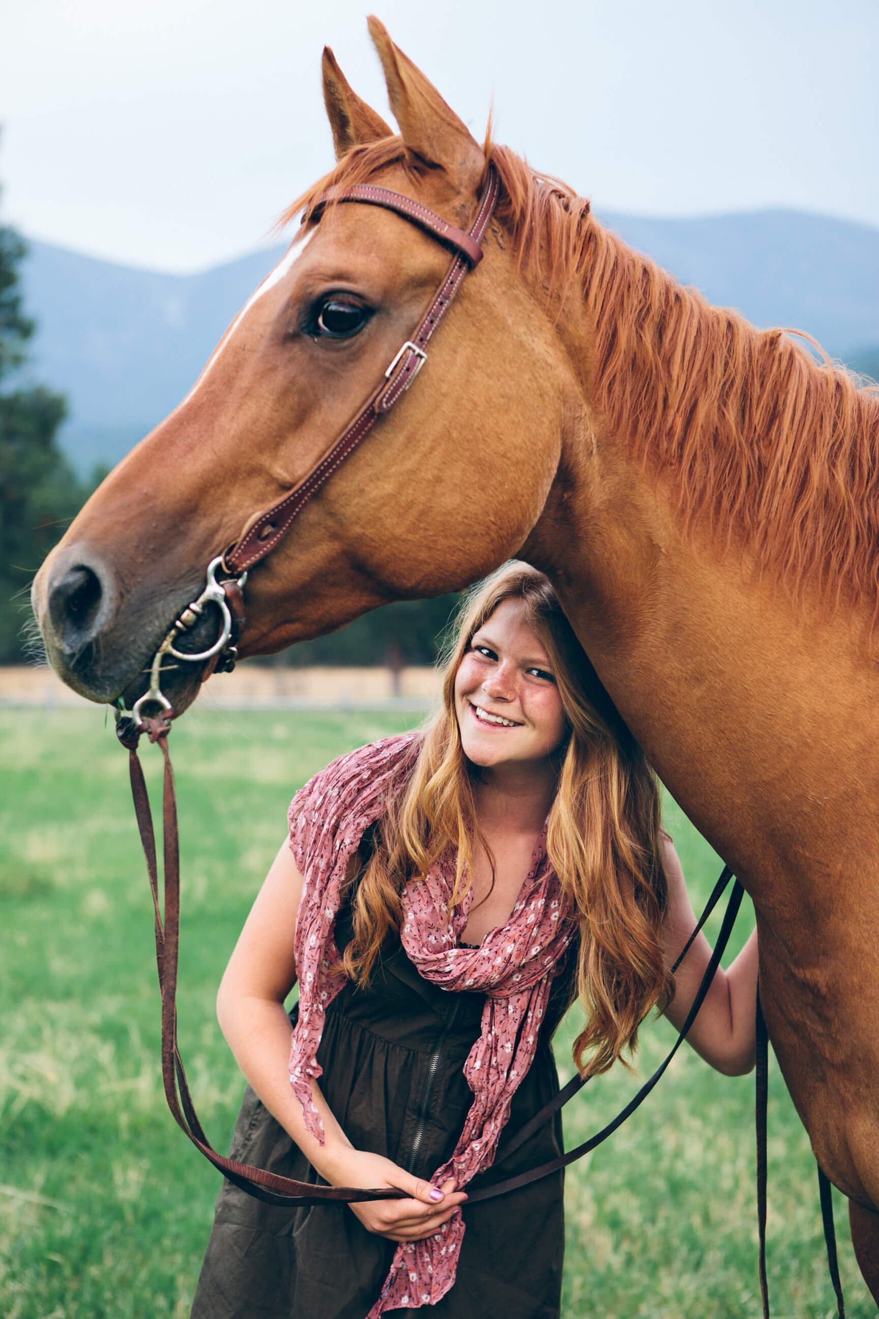 A senior girl smiles with her horse during her senior photos at Finley Point on Flathead Lake in Montana
