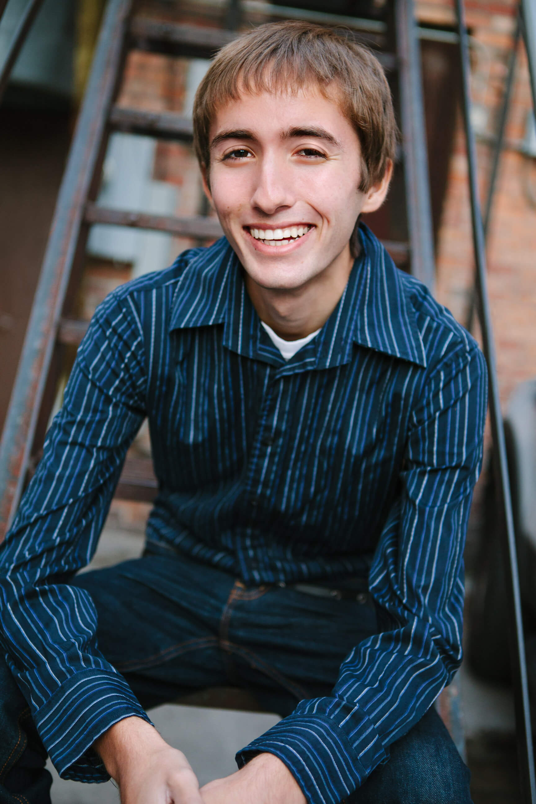 A senior boy sits on some stairs and smiles during his senior photos in Missoula Montana