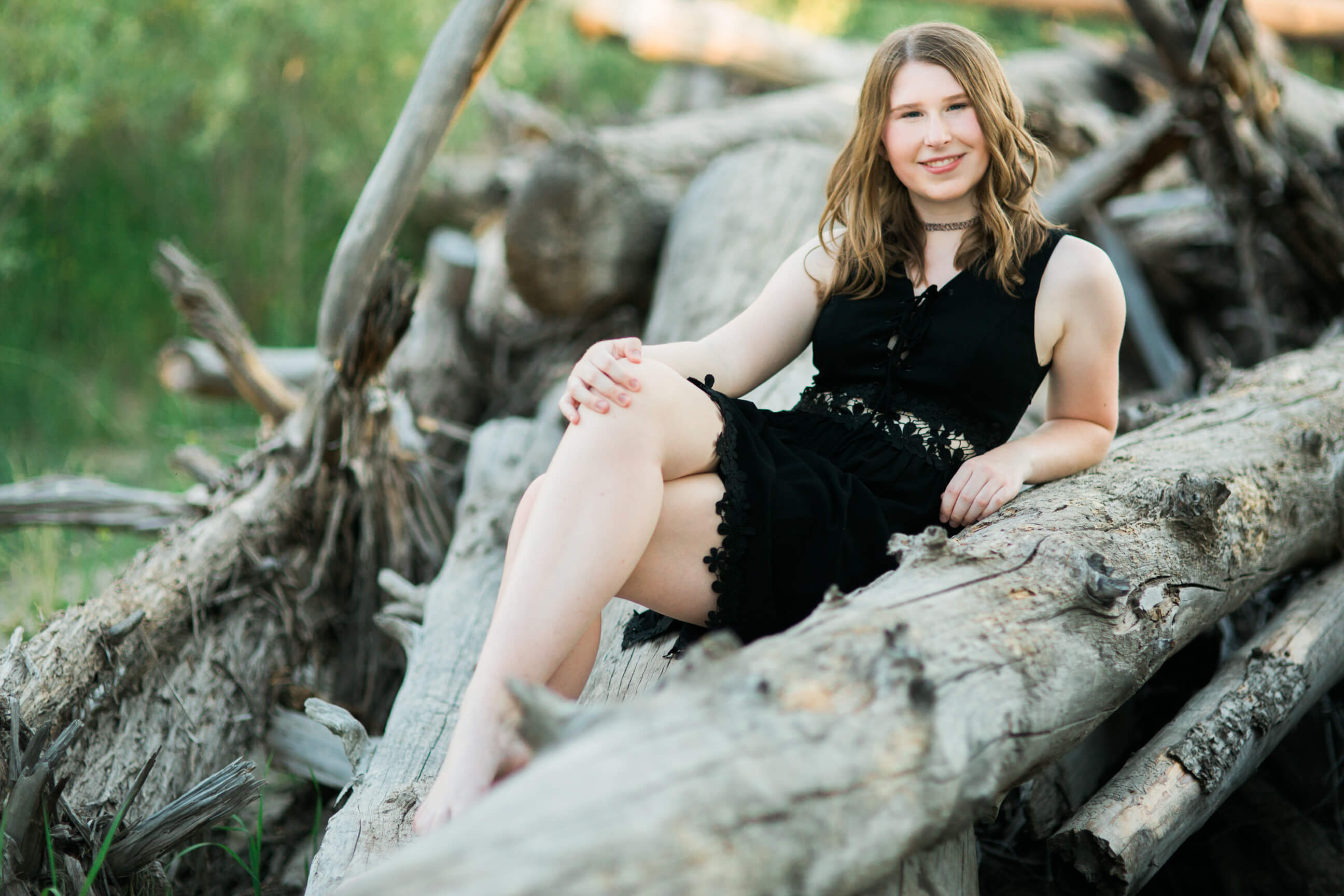 A senior girl sits on driftwood and smiles at the camera during her Missoula senior photos
