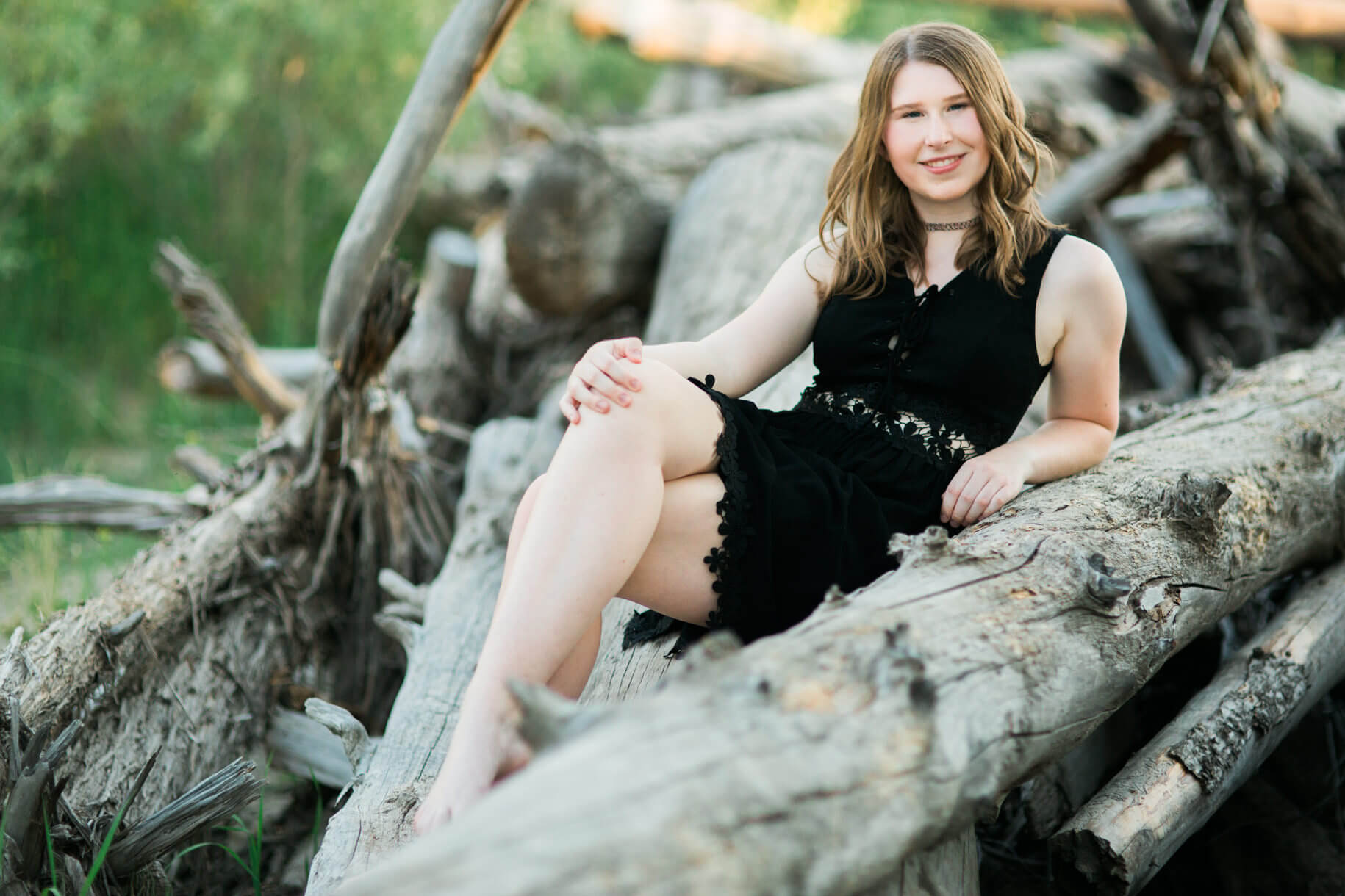 A high school senior girl sits on driftwood at her senior session in Missoula Montana