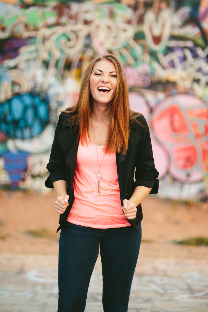 A high school senior girl laughs in front of a graffiti wall during her senior photos in Missoula Montana
