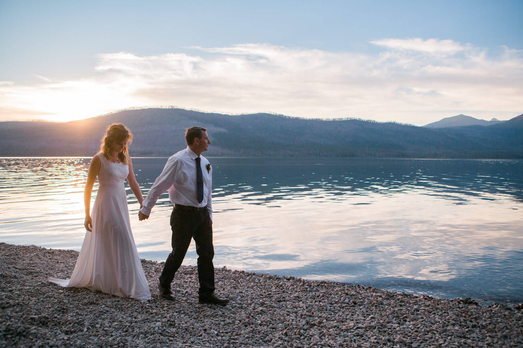 A bride and groom walk along the shoreline of Lake McDonald in Glacier National Park during their Montana elopement