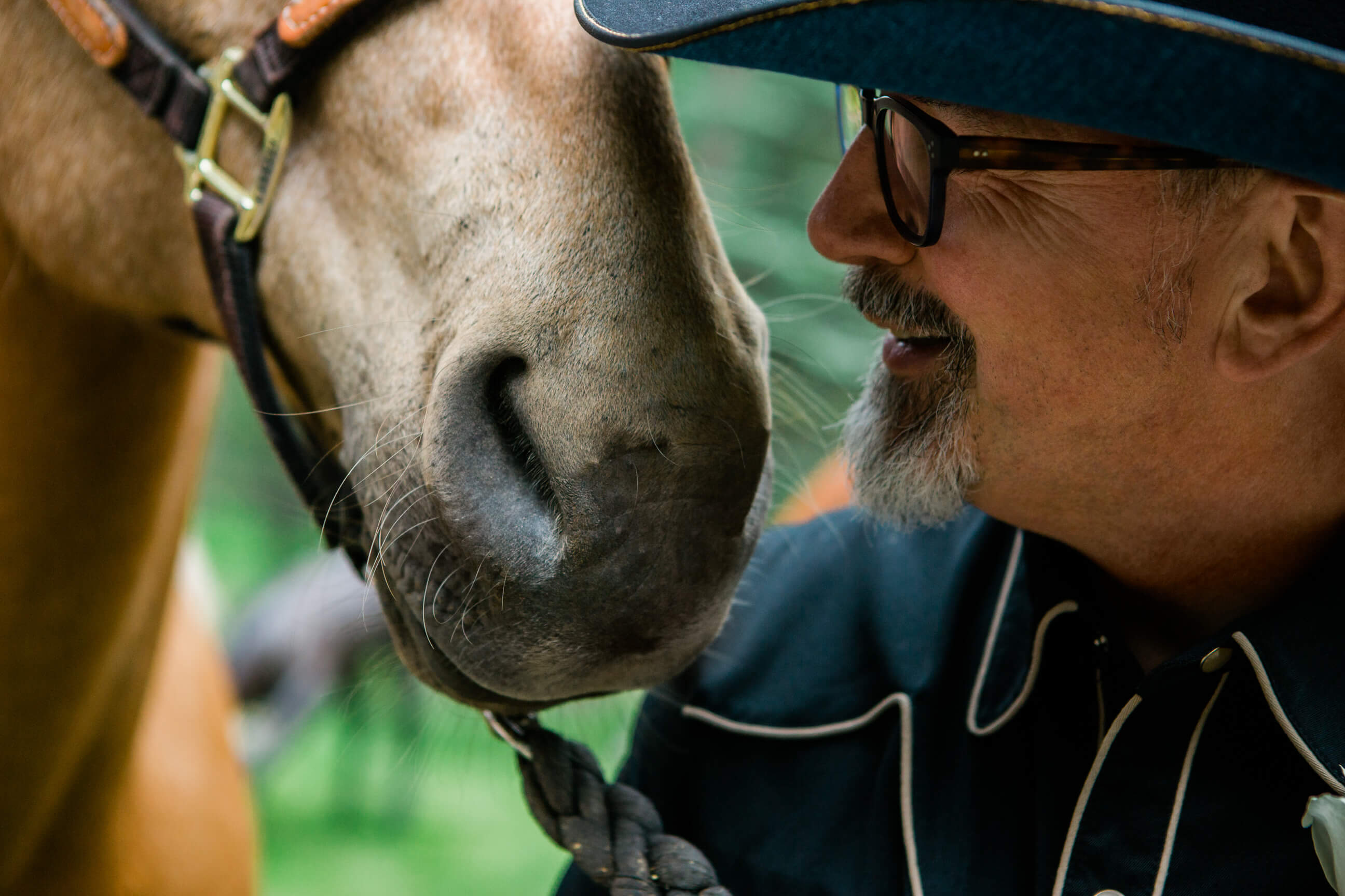 A groom stands next to a horse's nose during his elopement in Darby Montana