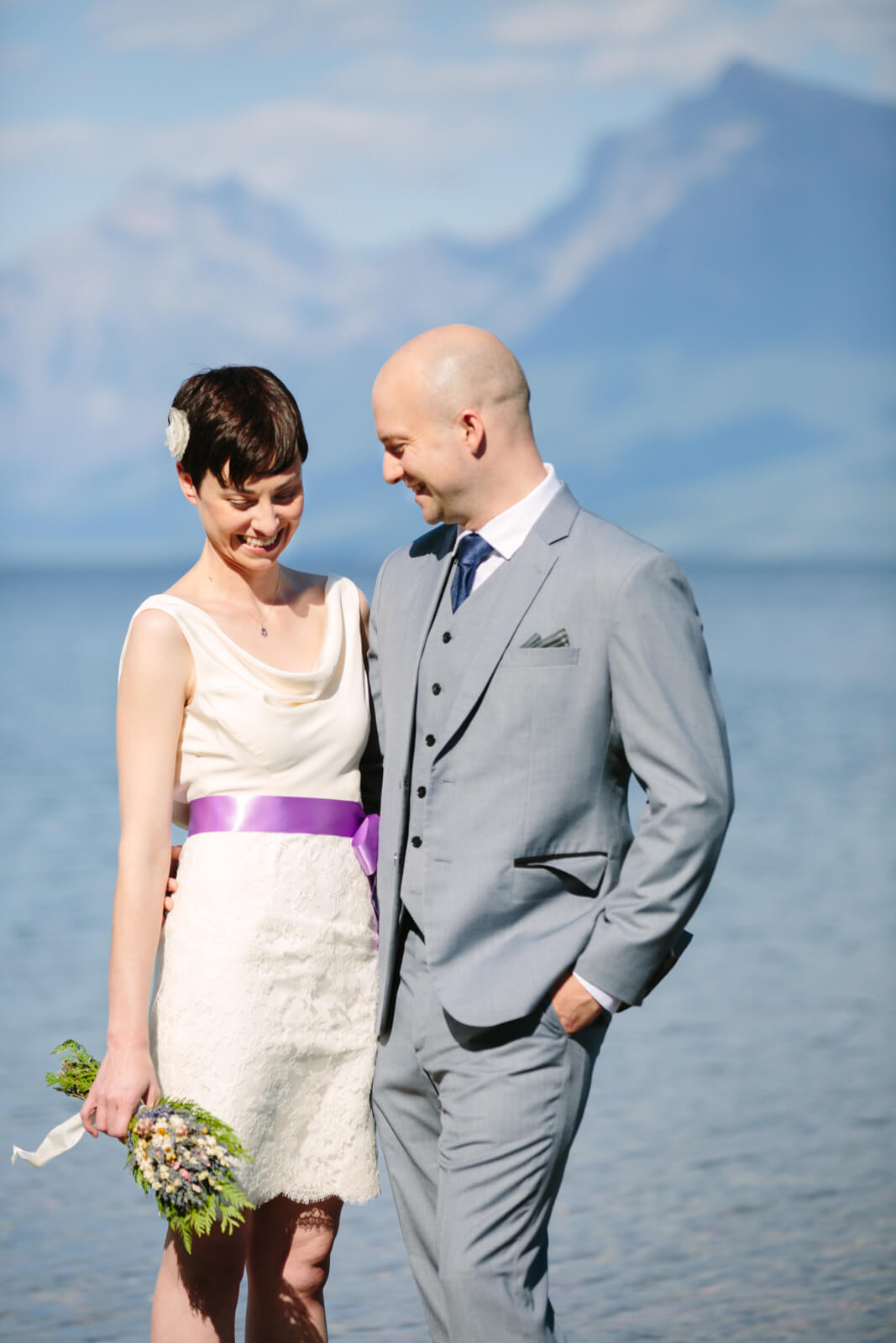 A bride and groom smile at one another at Lake McDonald at their Glacier National Park elopement